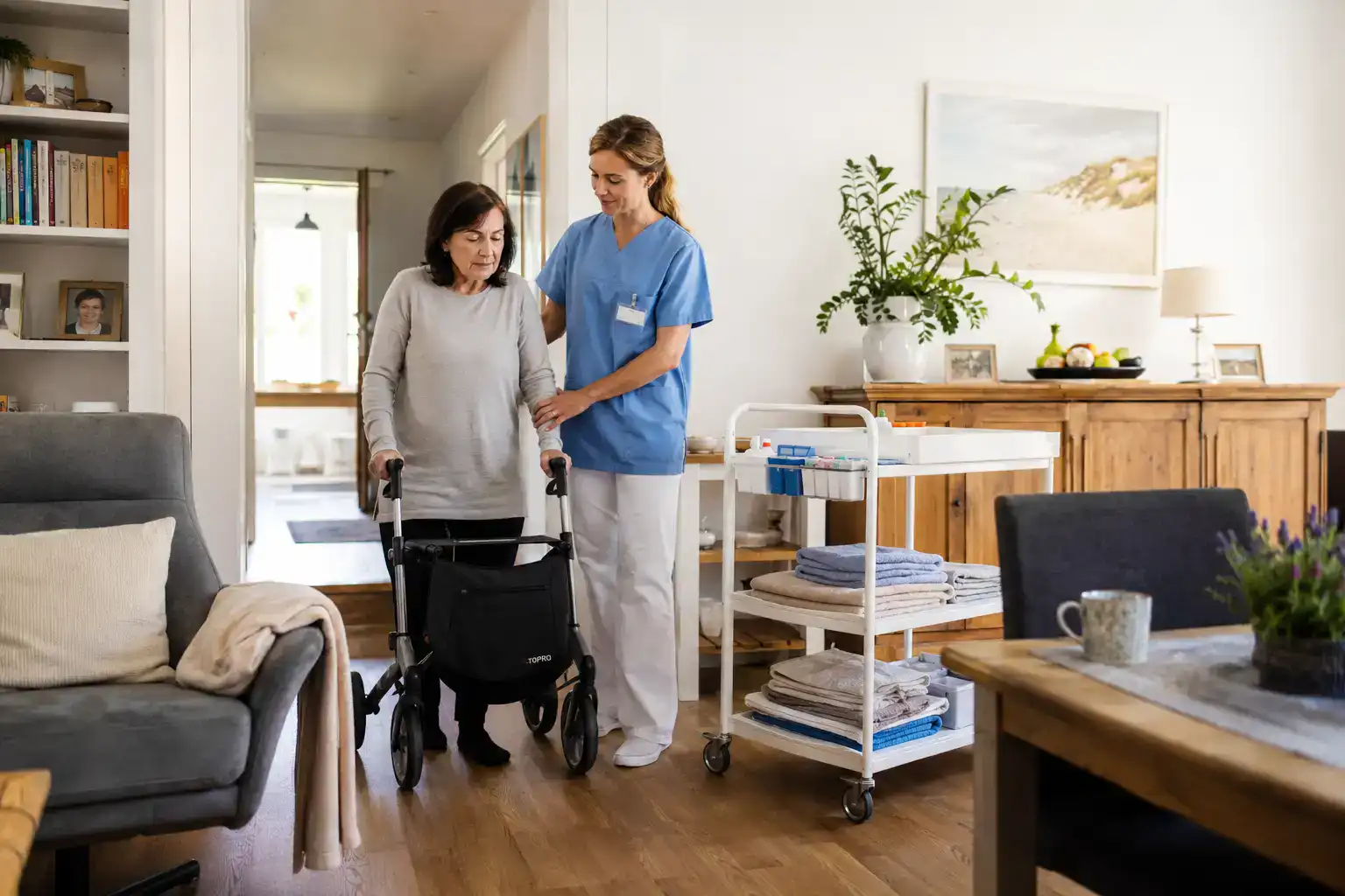 Pflegefachkraft unterstützt eine Patientin mit Morbus Pompe beim sicheren Gehen mit Rollator im häuslichen Umfeld.